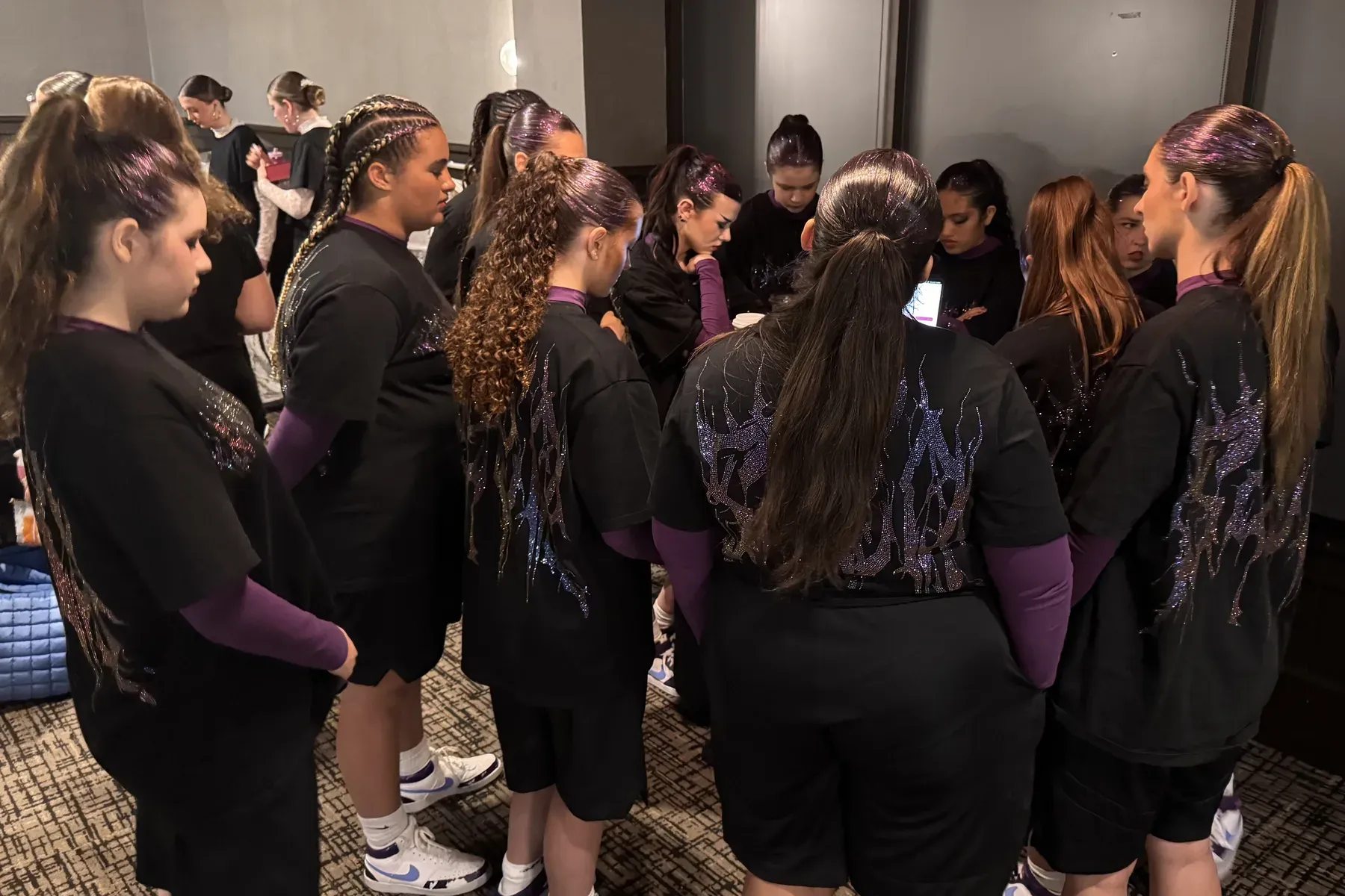 C3 dancers gathered backstage in costume, heads down before they compete