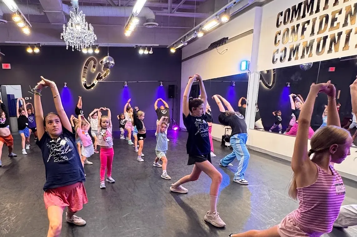 A C3 class stretching on the studio floor under the COMMITMENT CONFIDENCE COMMUNITY wall