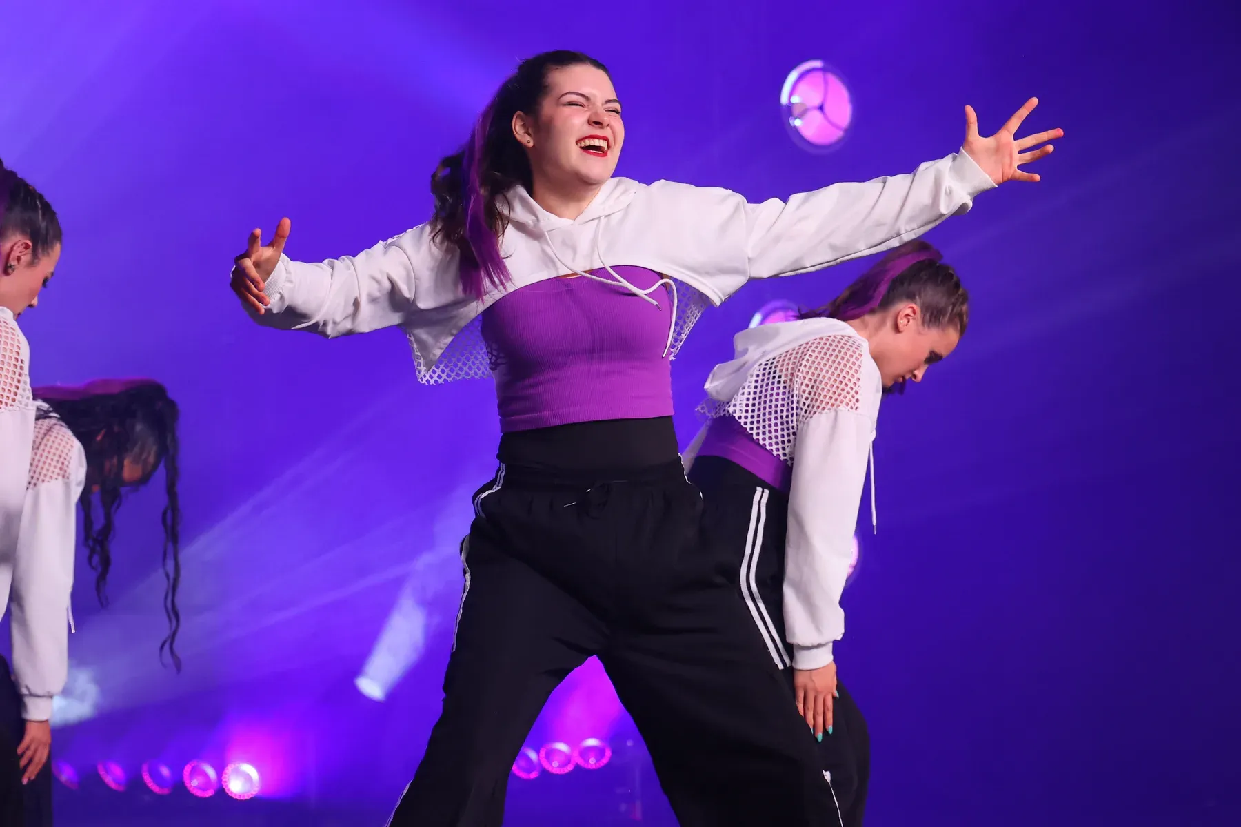 A C3 dancer laughing with her arms thrown wide mid-routine