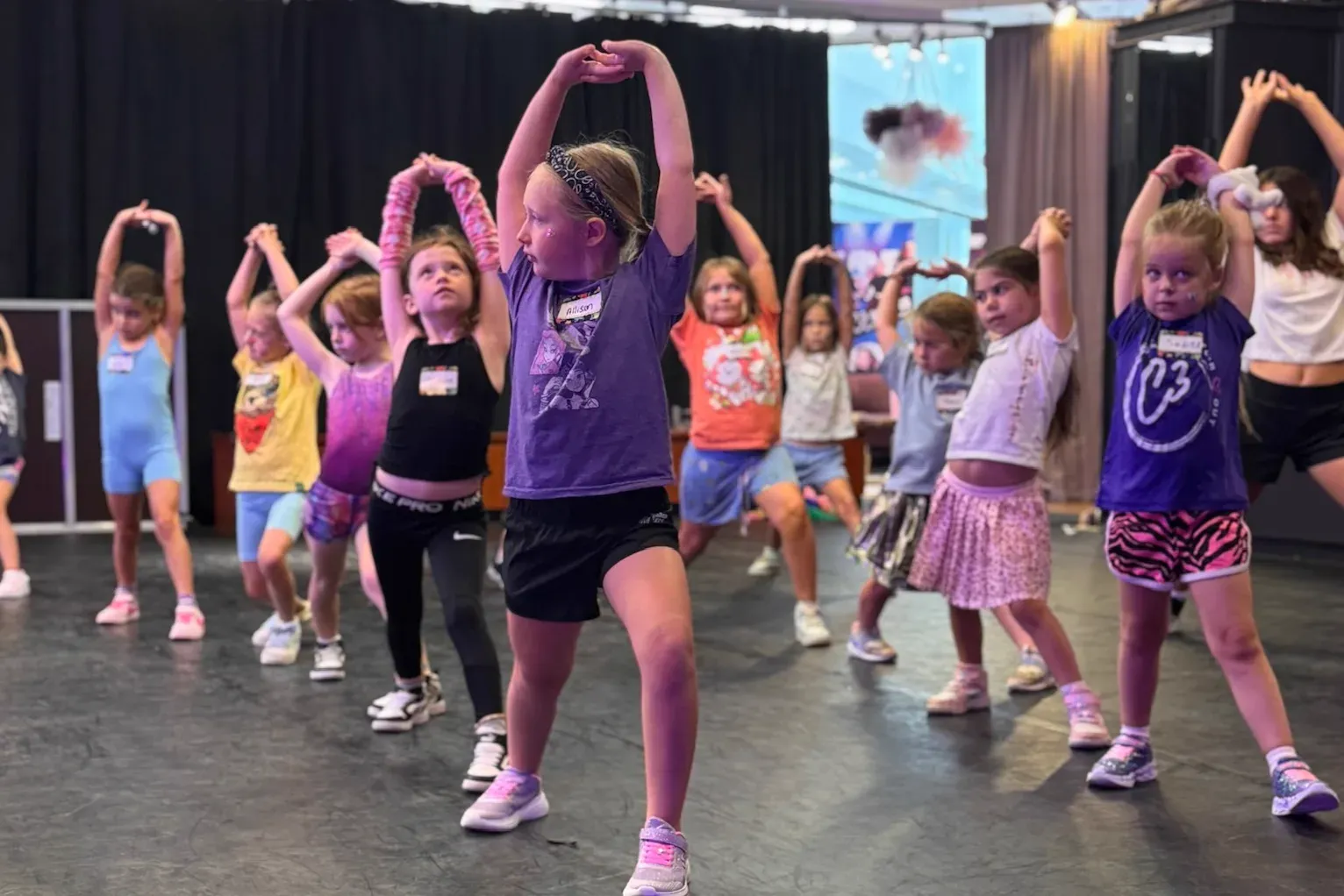 Young C3 dancers stretching in a warm-up line across the studio floor