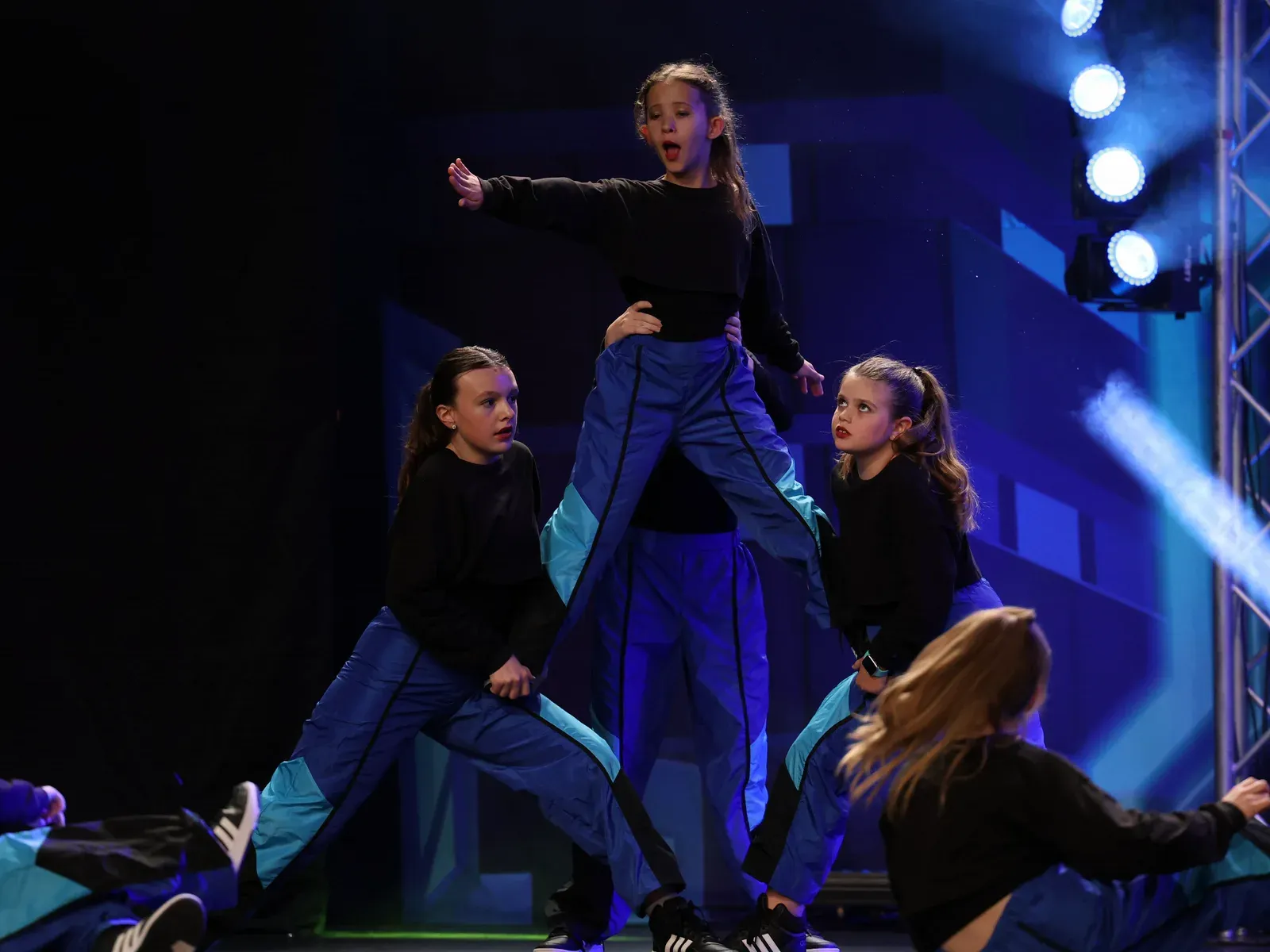 Young C3 dancers mid-routine on a blue-lit stage, one lifted above the group