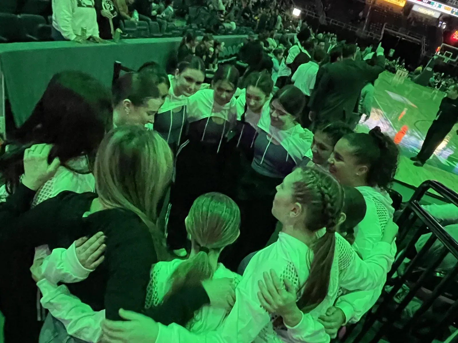 C3 dancers holding a huddle in the arena before they go on, lit green